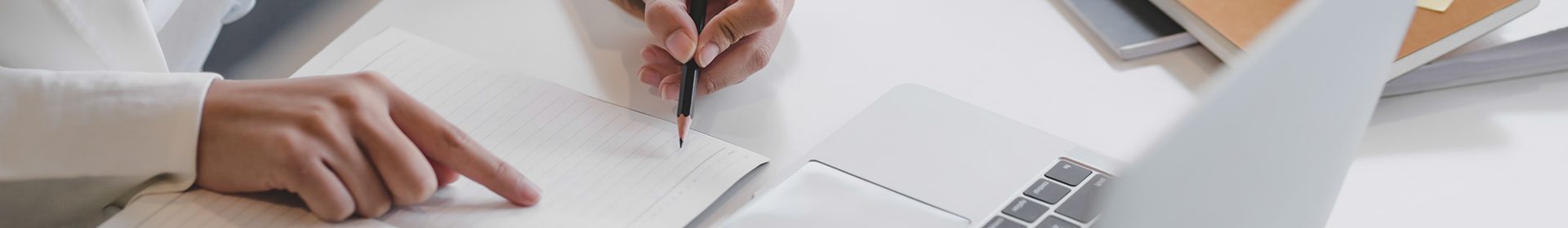 Cropped shot of businesswoman writing on notebook while working on laptop with office supplies on white table in office room